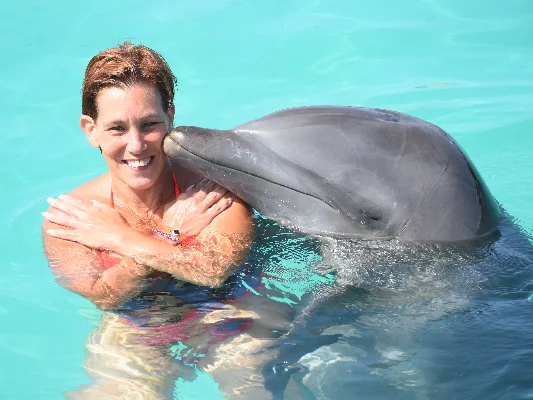 Manuela, glimlachend in het water terwijl een dolfijn haar zachtjes op de schouder kust.