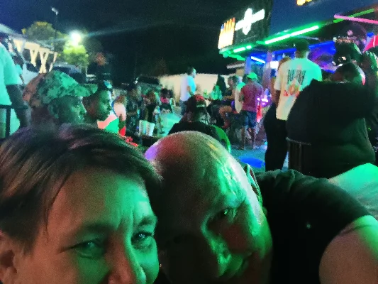 Manuela en Rainer maken een selfie voor een levendige locatie (karaoke) met kleurrijke lichten.