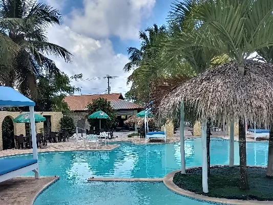 Zwembad van restaurant 'El Currican' in Juan Dolio, omgeven door palmbomen en parasols met uitzicht op het hoofdgebouw van het restaurant op de achtergrond.